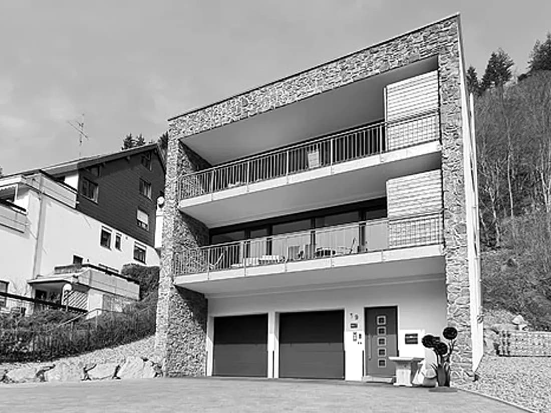 Dreigeschossiges Wohnhaus mit Natursteinfassade, umlaufenden Balkonen und zwei Garagen